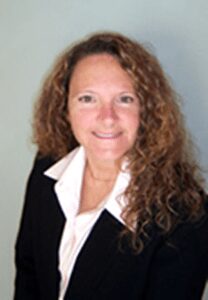 White woman with curly long hair in a white shirt and black blazer smiling